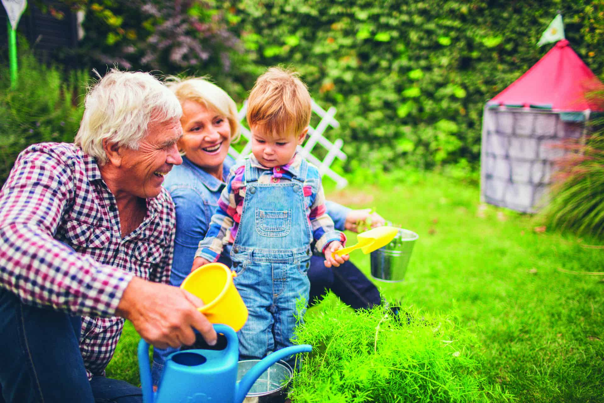 Kind mit Großeltern im Garten mit Schaufel, Eimer und Gießkanne